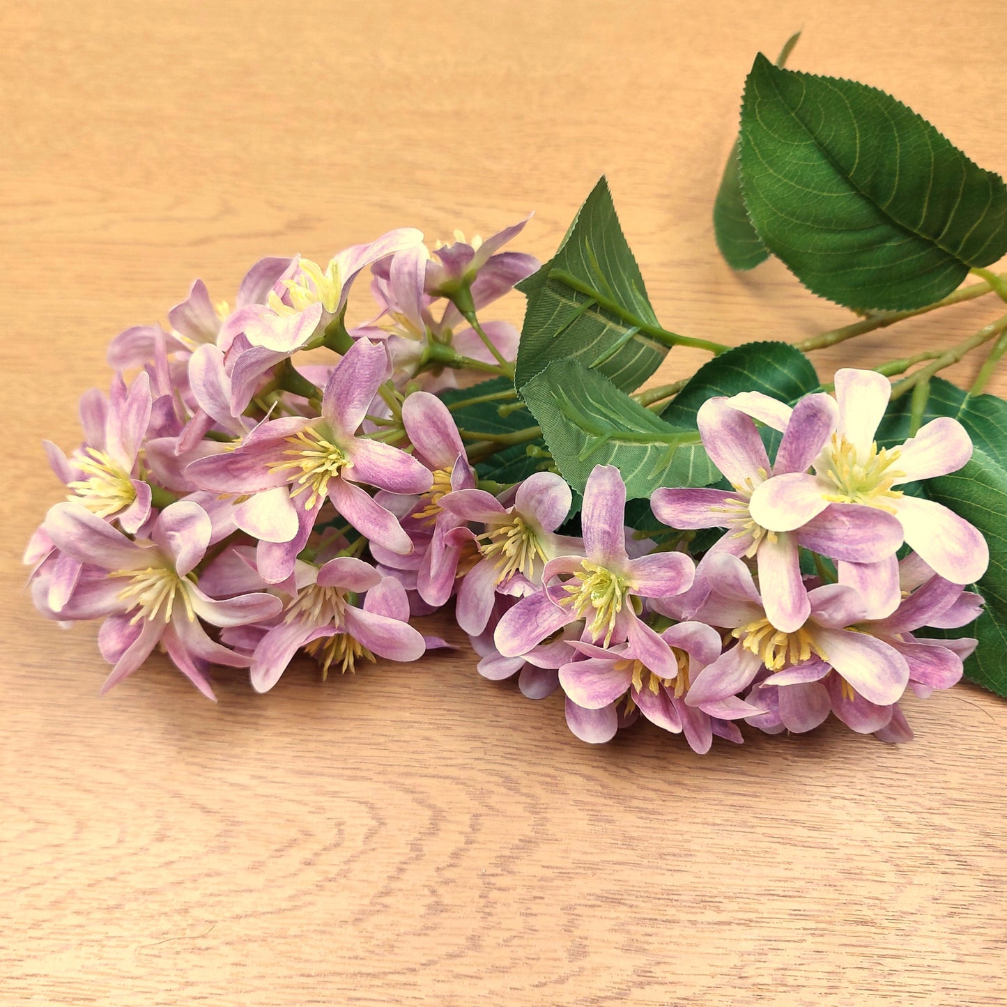 Bouquet of artificial pink Vernicia Tung Blossom flowers with green leaves on a wooden surface
