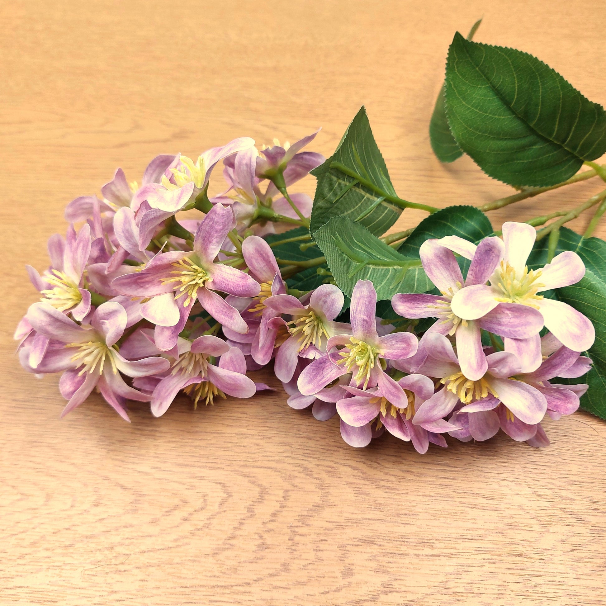 Bouquet of artificial pink Vernicia Tung Blossom flowers with green leaves on a wooden surface