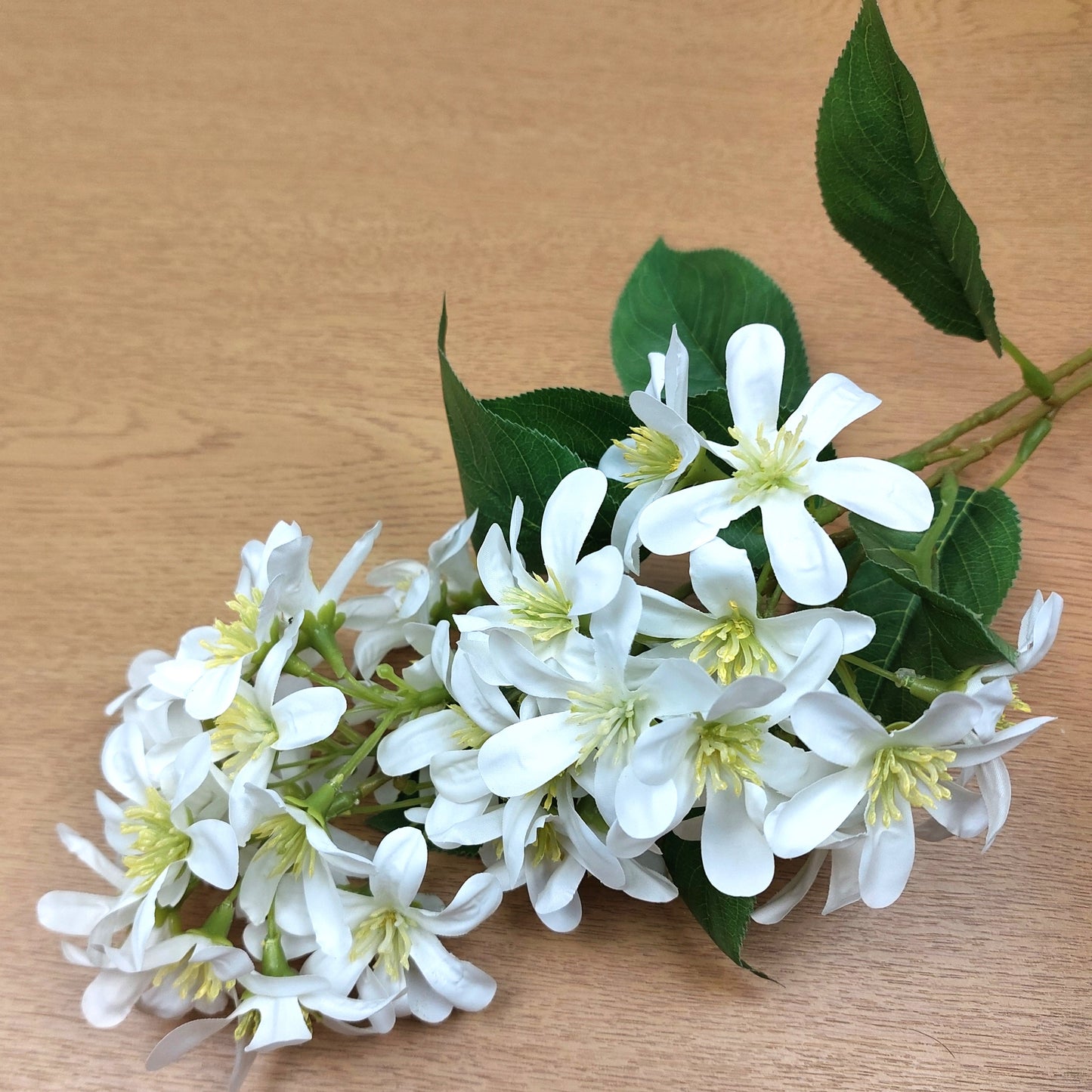 Bouquet of artificial white Vernicia Tung Blossom flowers with green leaves on a wooden surface