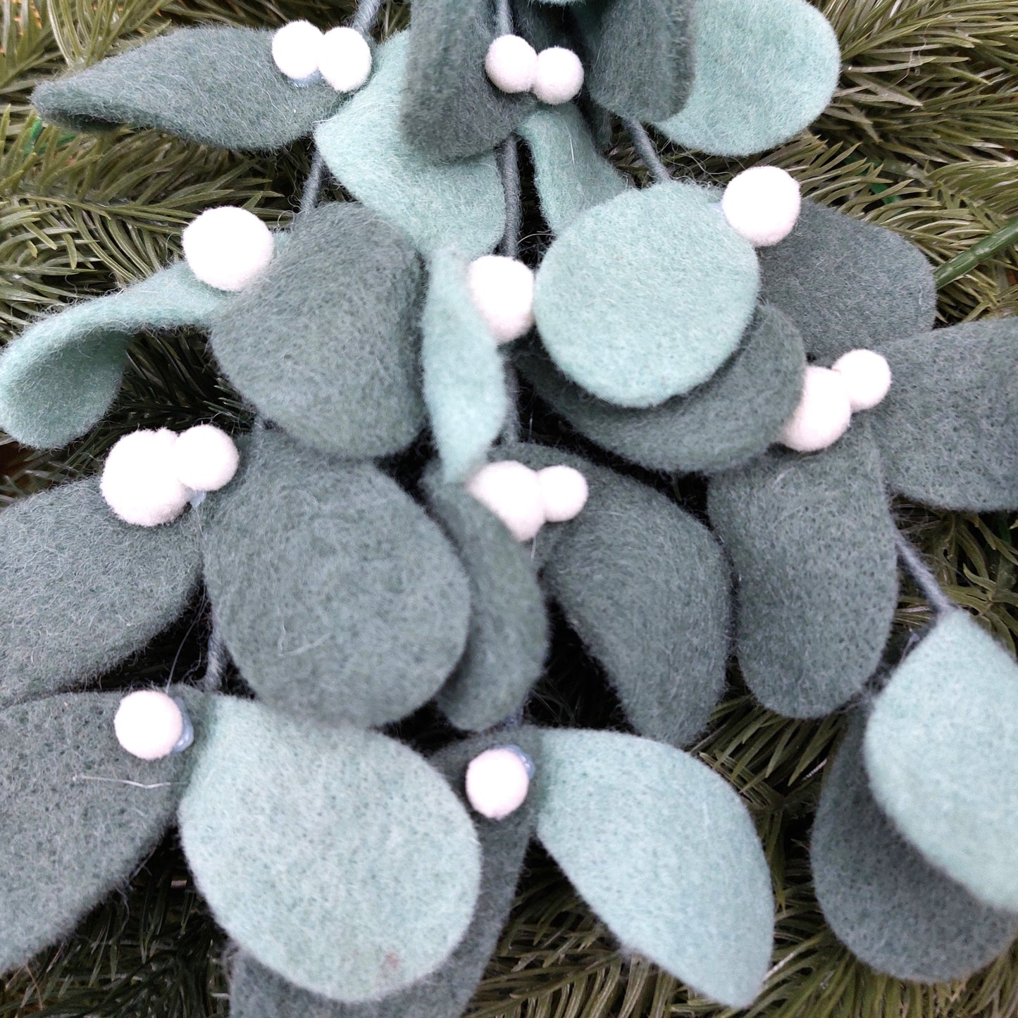 Decorative felt mistletoe hanging decoration with green leaves and white berries on a natural background
