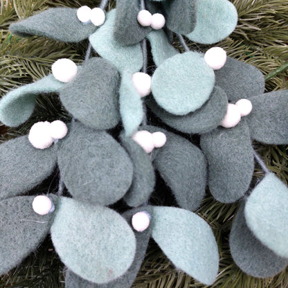 Decorative felt mistletoe hanging decoration with green leaves and white berries on a natural background