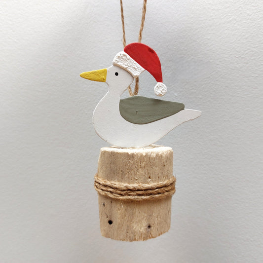 A metal seagull wearing a christmas hat on a wooden groyne against a grey background