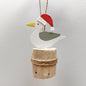 A metal seagull wearing a christmas hat on a wooden groyne against a grey background