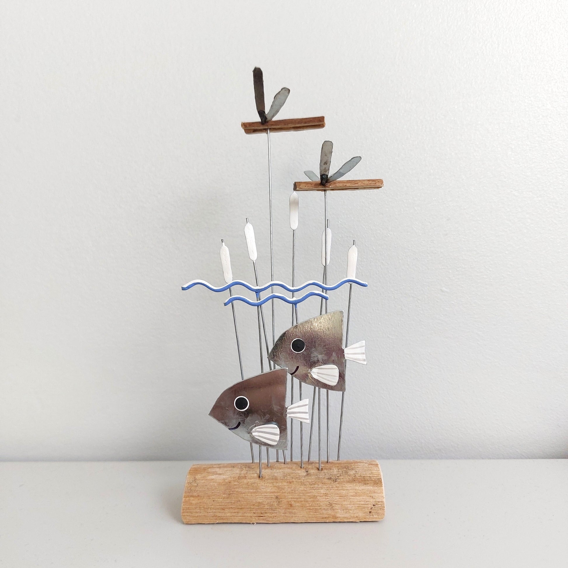 Decorative sculpture of fish on a stand with a wavy line design against a plain background