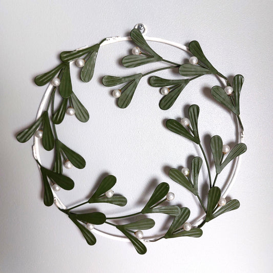 Decorative metal wreath made of green leaves and white berries on a light gray background