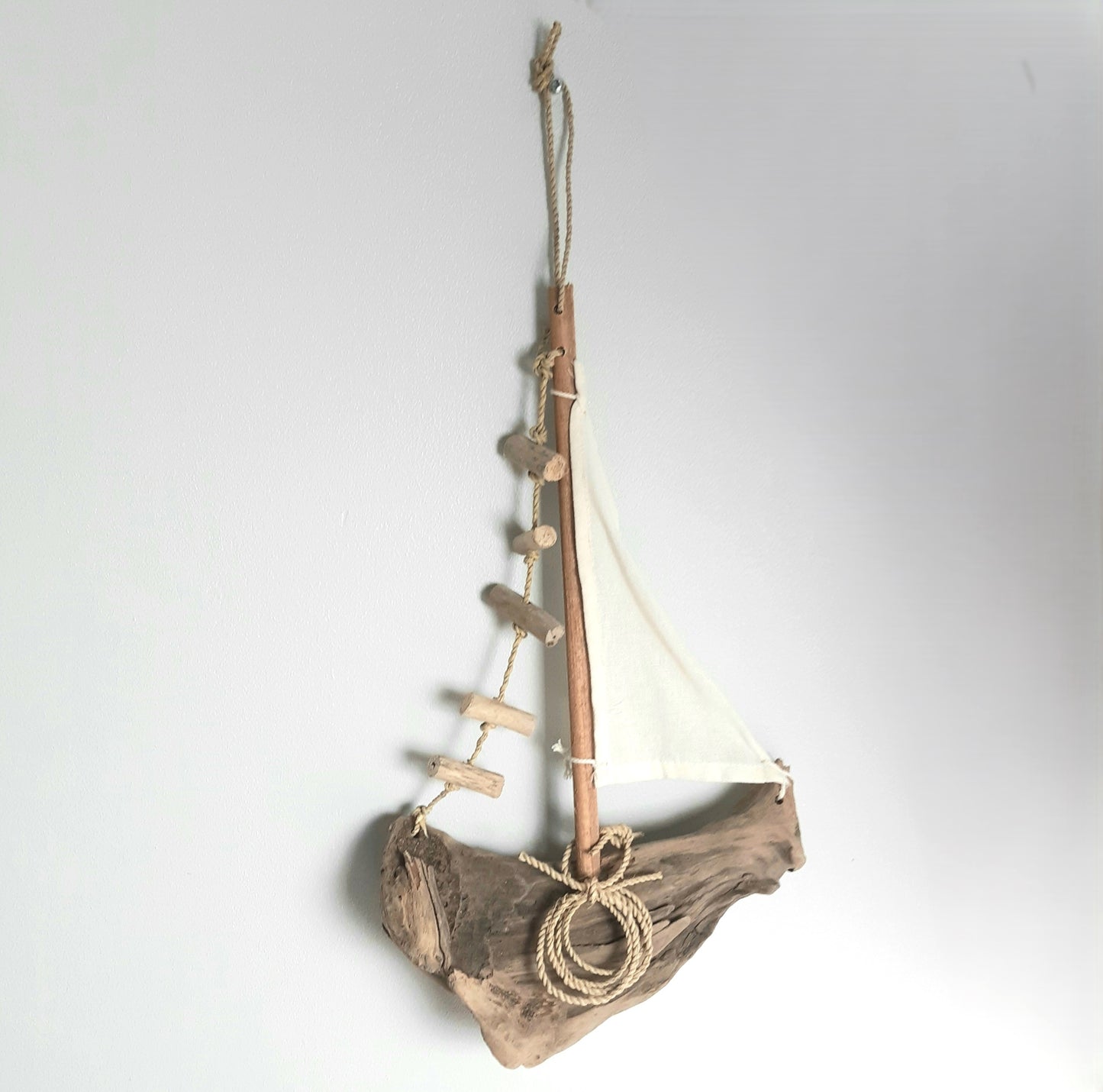 Decorative sailboat made of driftwood with a white sail on a plain background