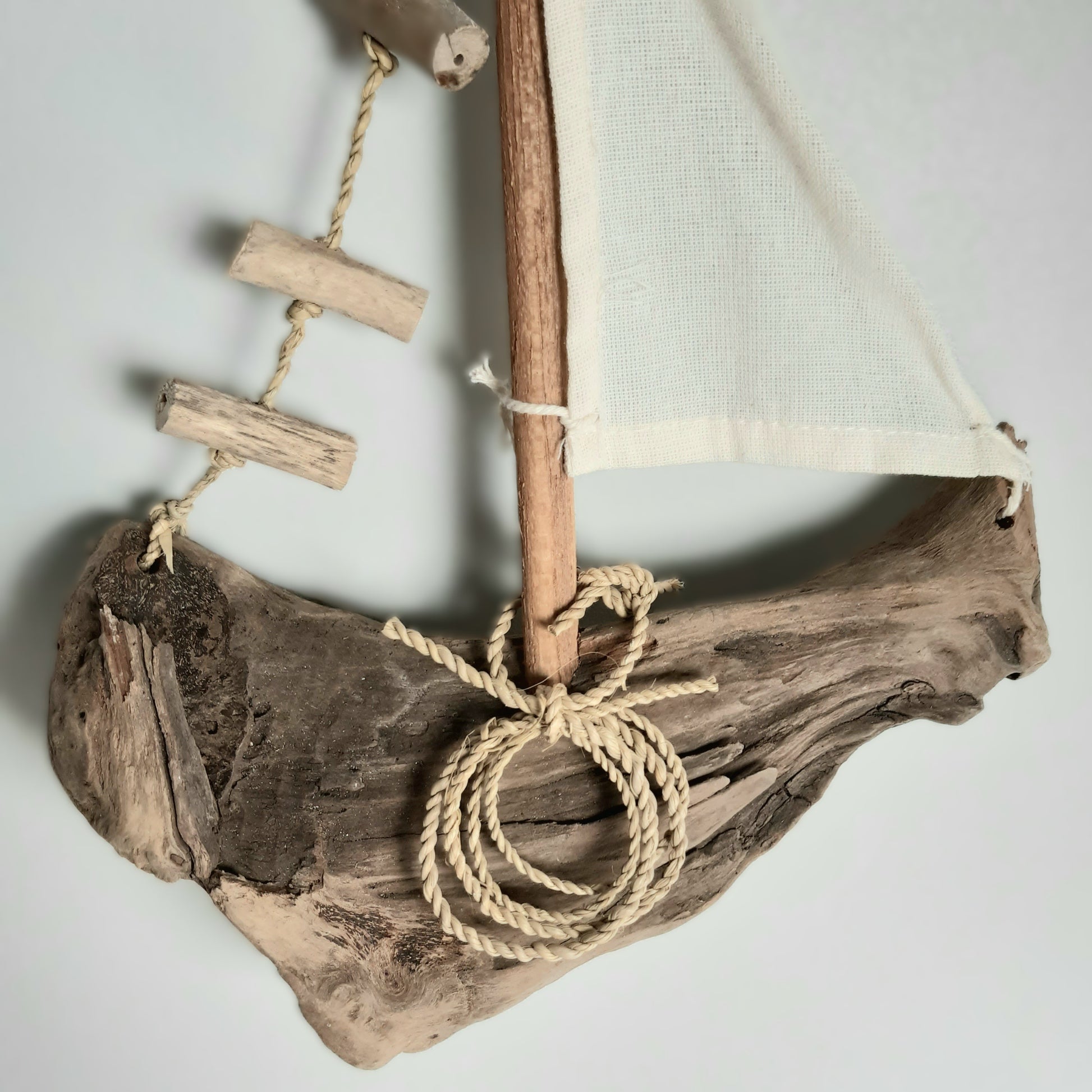 Driftwood sailboat with a white sail on a plain background