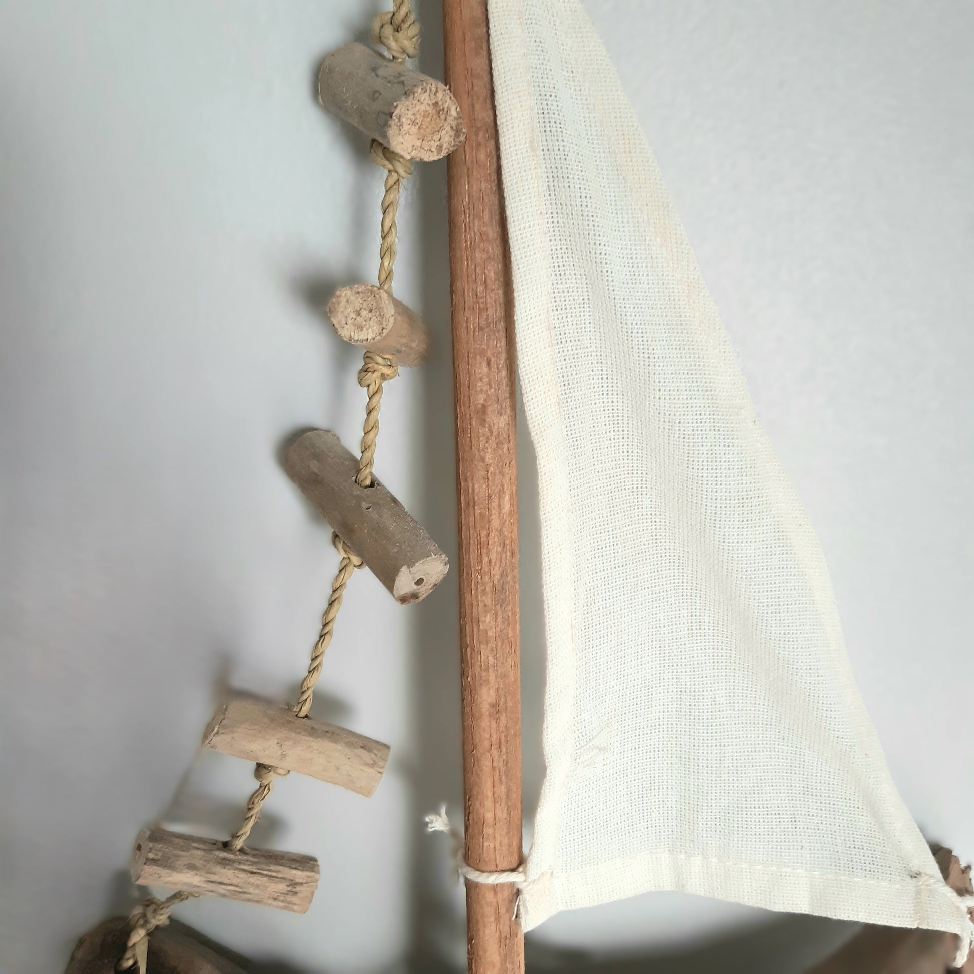 Sailboat model with a wooden mast, rope, and fabric sail against a light background