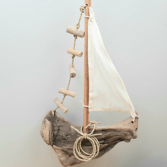 Decorative sailboat made from driftwood with a white sail on a light gray background
