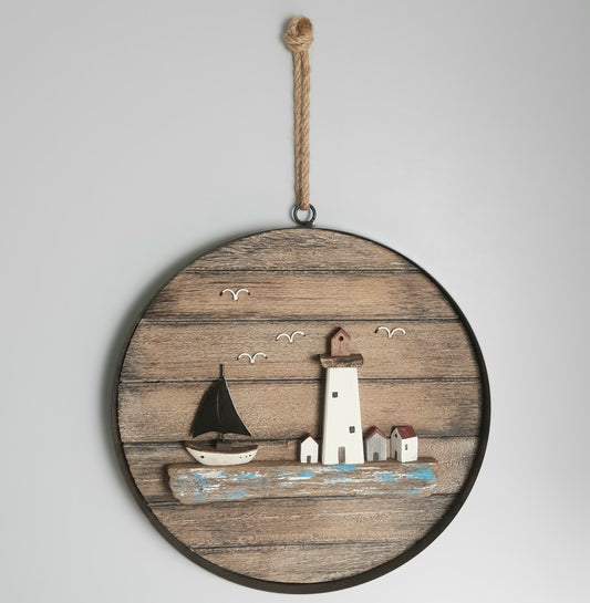 Decorative wall art with a lighthouse and sailboat on a wooden circle, hanging against a light gray background.
