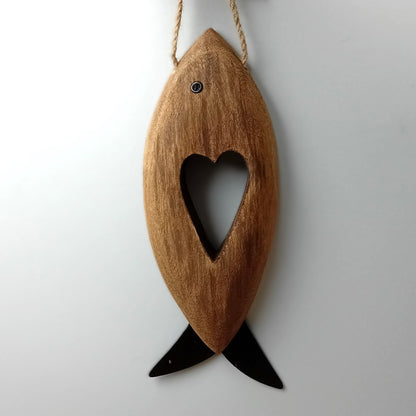 A brown wooden carved fish with metal fins and eye, with a heart shape carved in the middle hanging from a jute rope against a pale background.