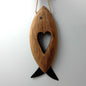 A brown wooden carved fish with metal fins and eye, with a heart shape carved in the middle hanging from a jute rope against a pale background.