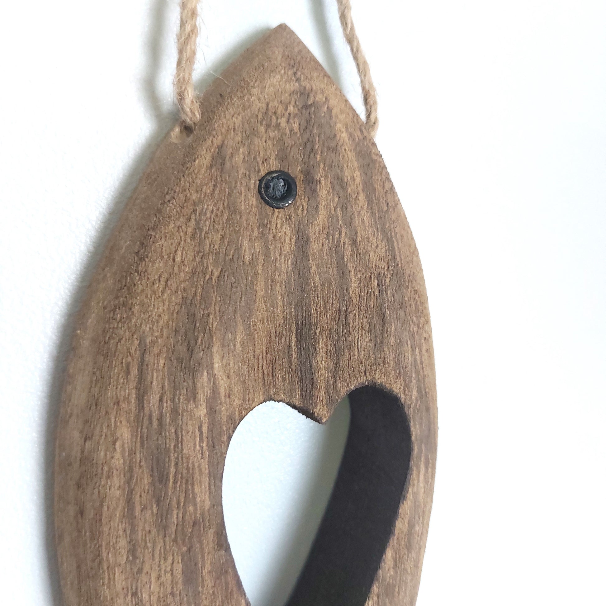 Wooden fish-shaped ornament with a heart shape cut out hanging with a rope on a white background