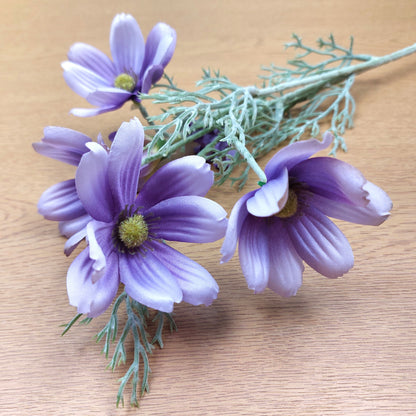 Artificial Lilac Cosmos Stems with green-yellow centers and dusty green foliage, arranged on a light wood surface.