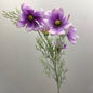 Artificial Purple cosmos-style flowers with Lilac to lavender petals and yellow centers, arranged with green feathery stems against a plain light gray background.