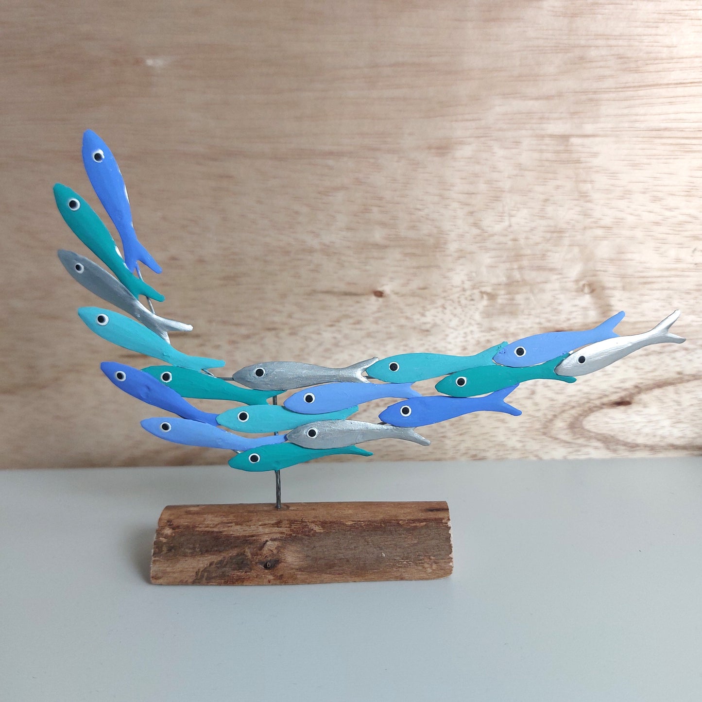 Decorative metal sculpture of blue and green fish on a wooden base against a wooden background