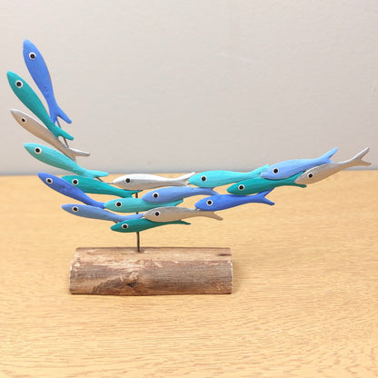 Decorative metal hand painted sculpture of blue and green fish on a wooden base against a light background