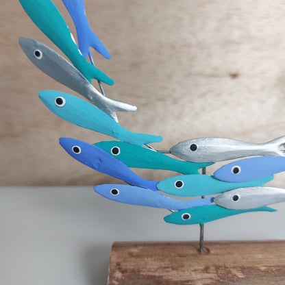 Close up of hand painted colourful blue, green and silver fish mounted on a wooden base against a pale background.