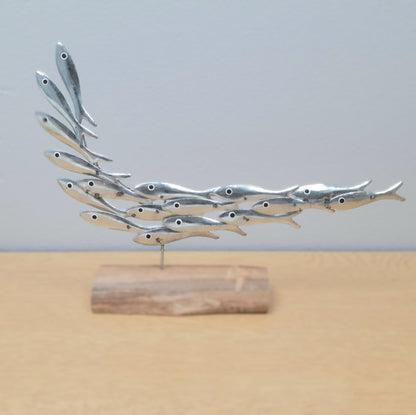 Metallic fish sculpture on a wooden base against a light gray background