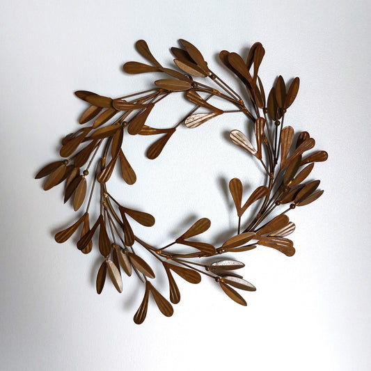 An ornate metal red/brown bronze leafy mistletoe wreath against a plain background