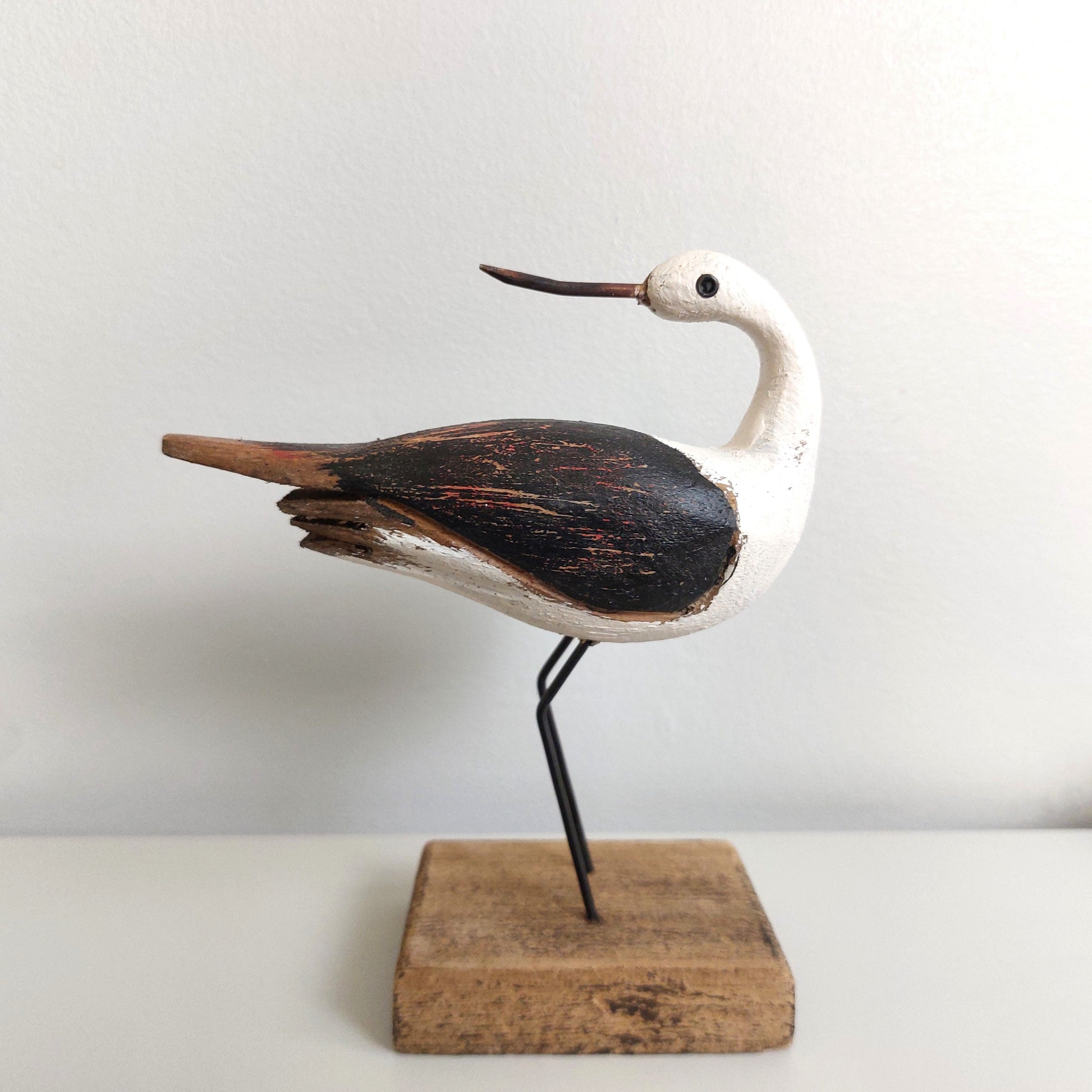 Wooden bird sculpture on a stand with a plain background