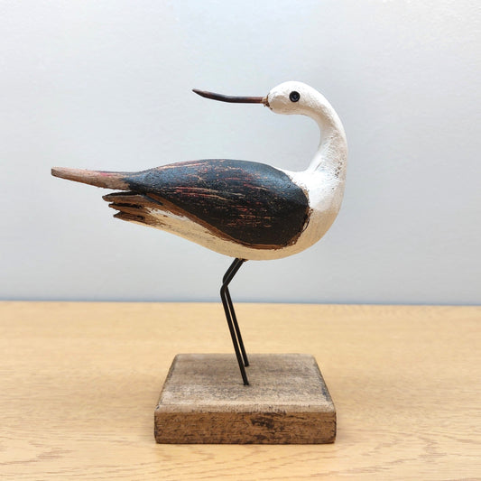 Wooden bird sculpture on a stand against a light gray background