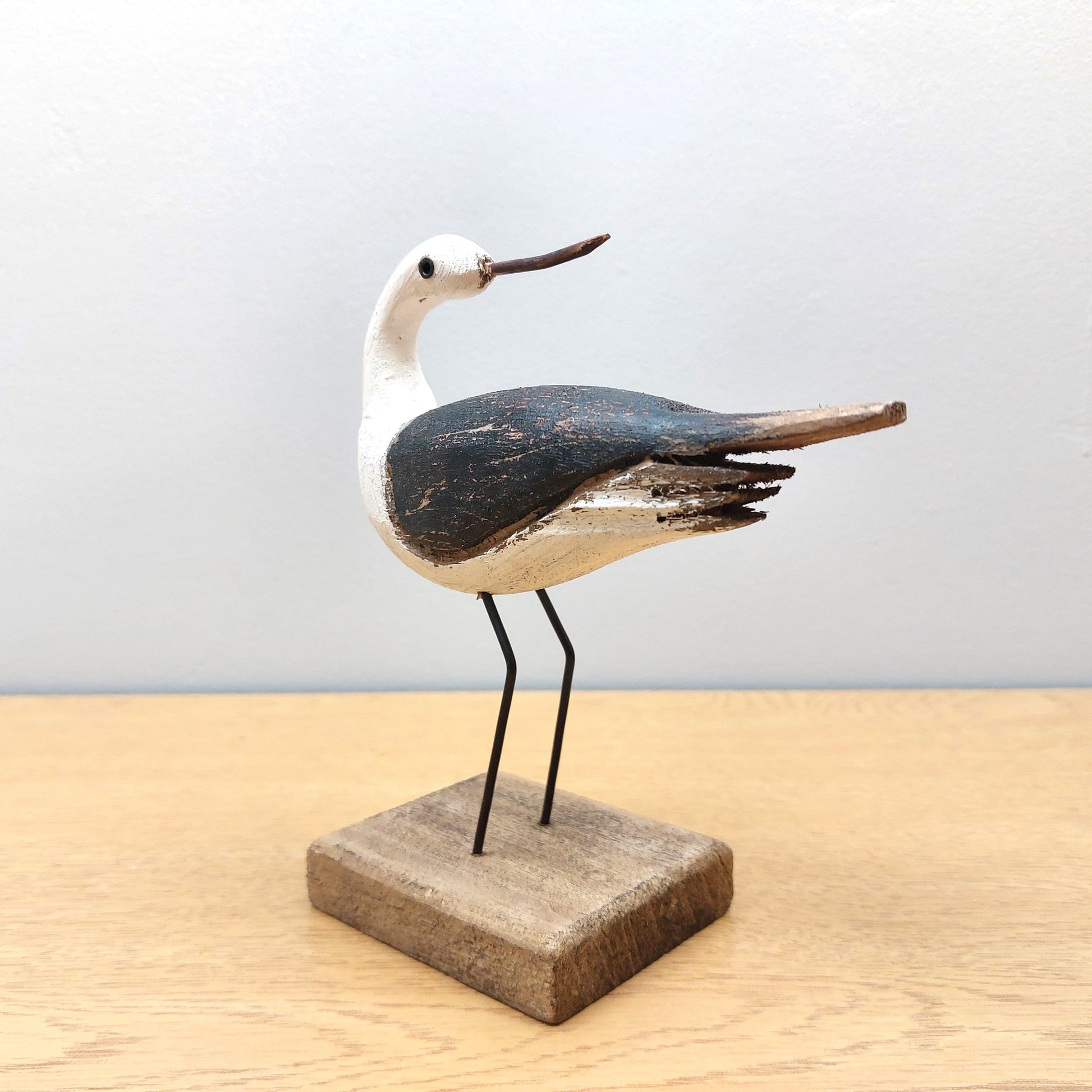 Wooden bird sculpture on a stand against a light background