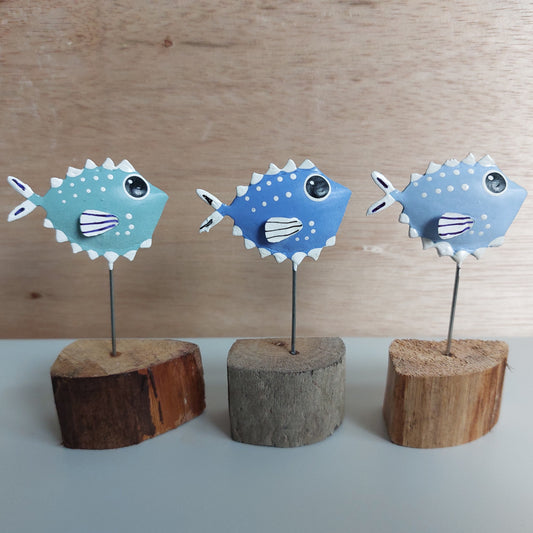 A set of three painted metallic puffer fish on wooden blocks against a wooden background