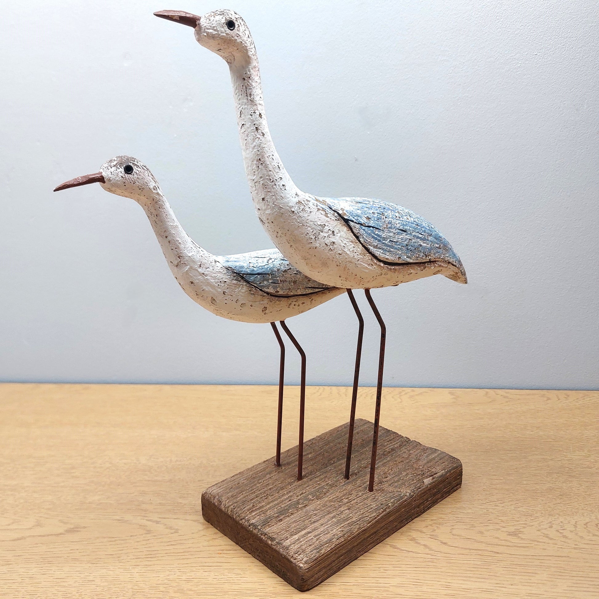 Two wooden wading birds on a wooden base against a light background