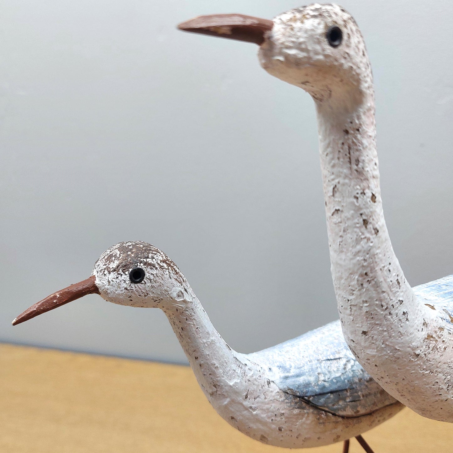 A close up of two wooden wading birds with speckled patterns on a neutral background