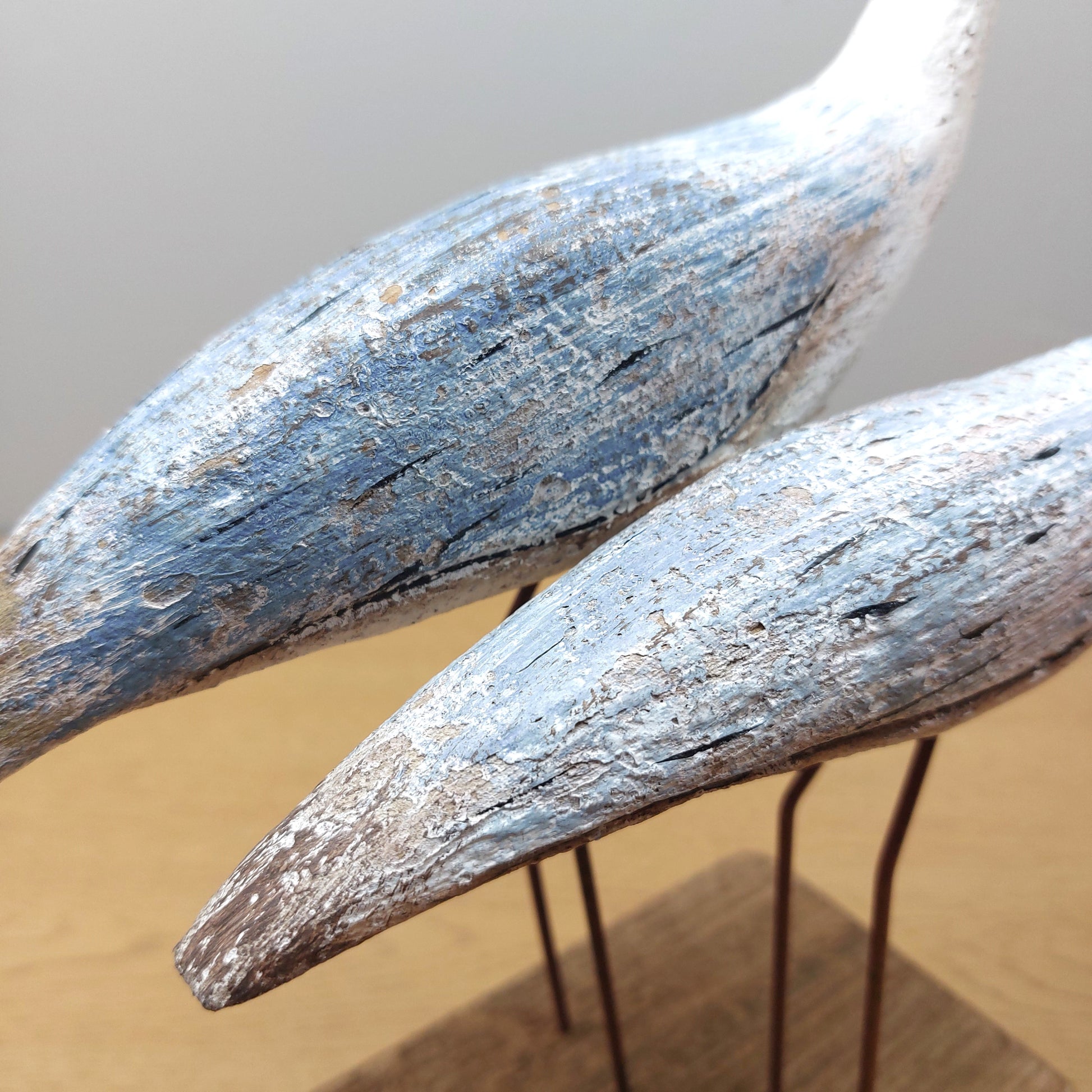 A close up of Two wooden wading birds with a rustic finish on a neutral background
