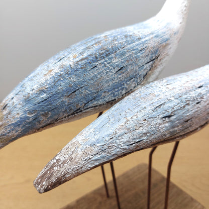A close up of Two wooden wading birds with a rustic finish on a neutral background