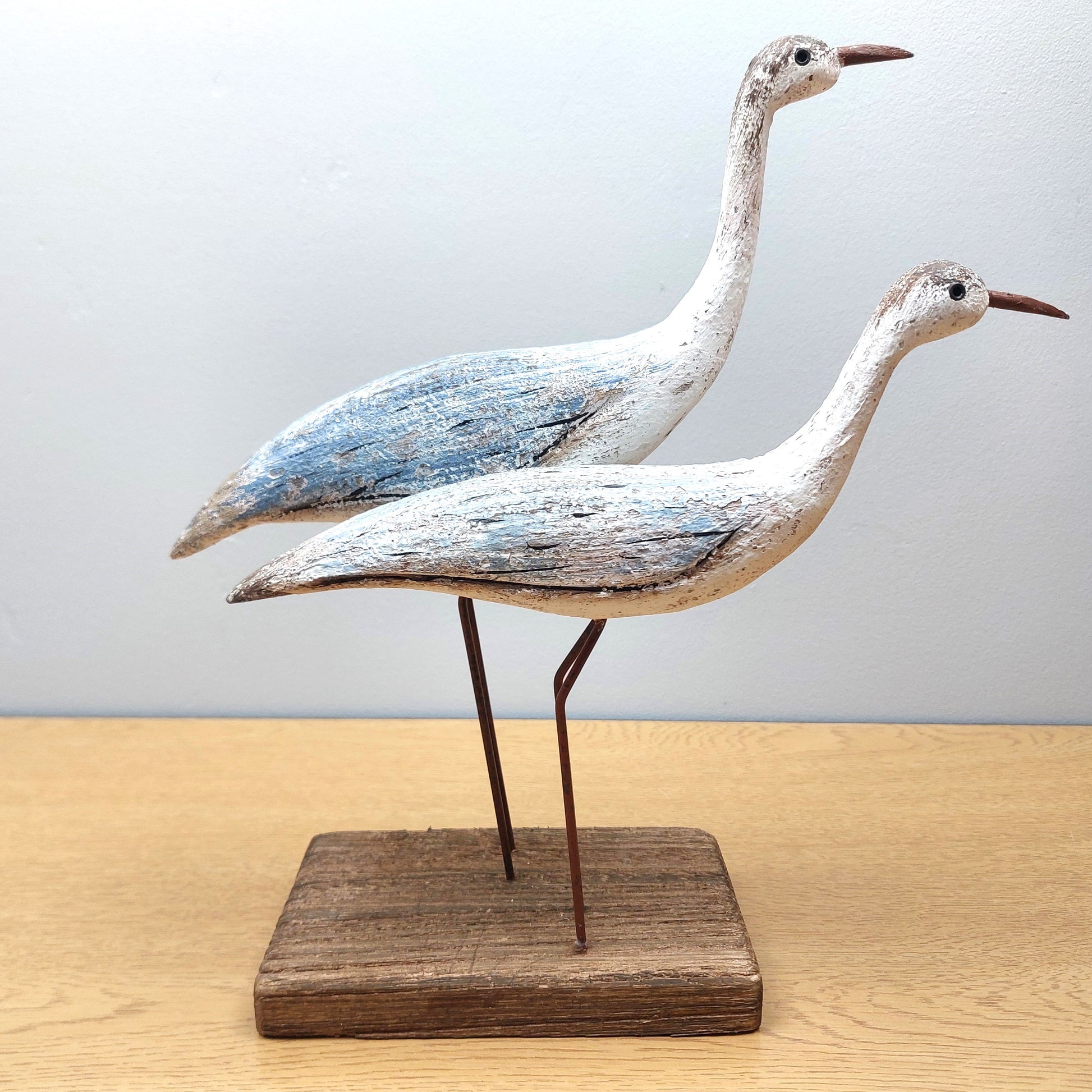 Two wooden bird sculptures on a stand against a light background