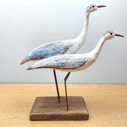Two wooden bird sculptures on a stand against a light background
