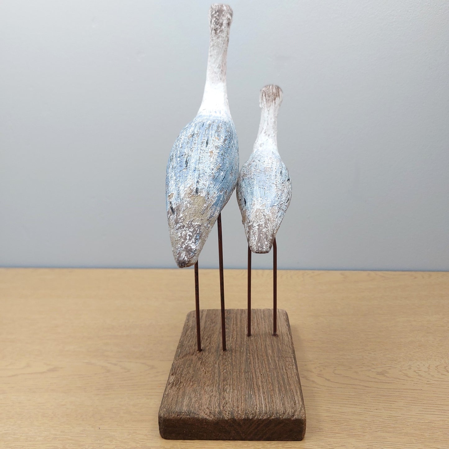 Two wooden wading birds facing away on a wooden stand against a gray background