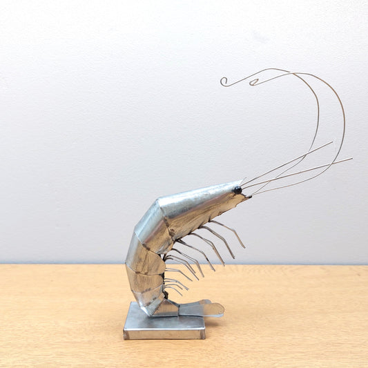 Metal prawn sculpture on a wooden table against a grey background