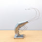 Metal prawn sculpture on a wooden table against a grey background