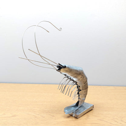 Metallic shrimp sculpture on a wooden surface with a plain background
