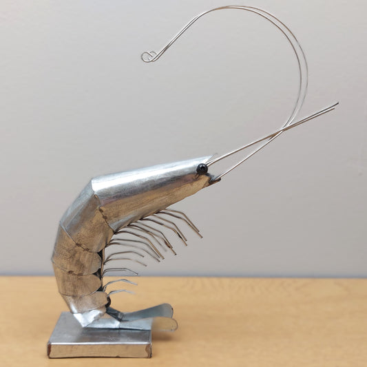 A metal prawn figurine on a wooden surface against a pale blue background