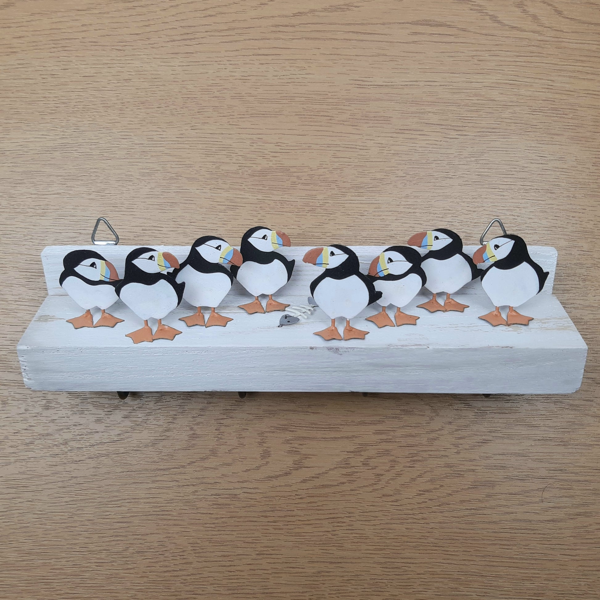 Decorative shelf with metal painted puffins and a fish skeleton on a wooden surface