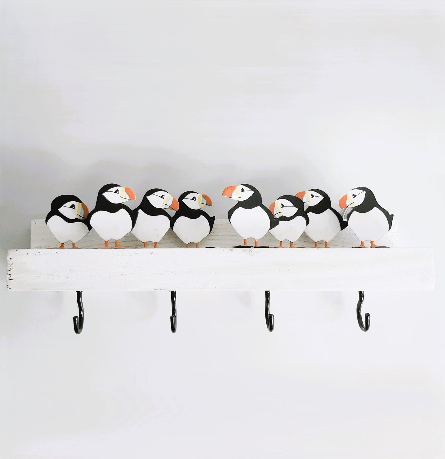 Decorative shelf with puffin-shaped figures and hooks on a plain background