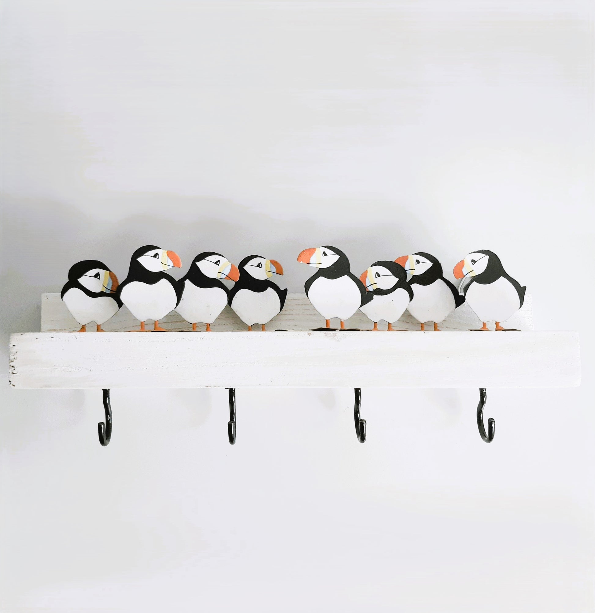 Decorative shelf with puffin-shaped figures and hooks on a plain background