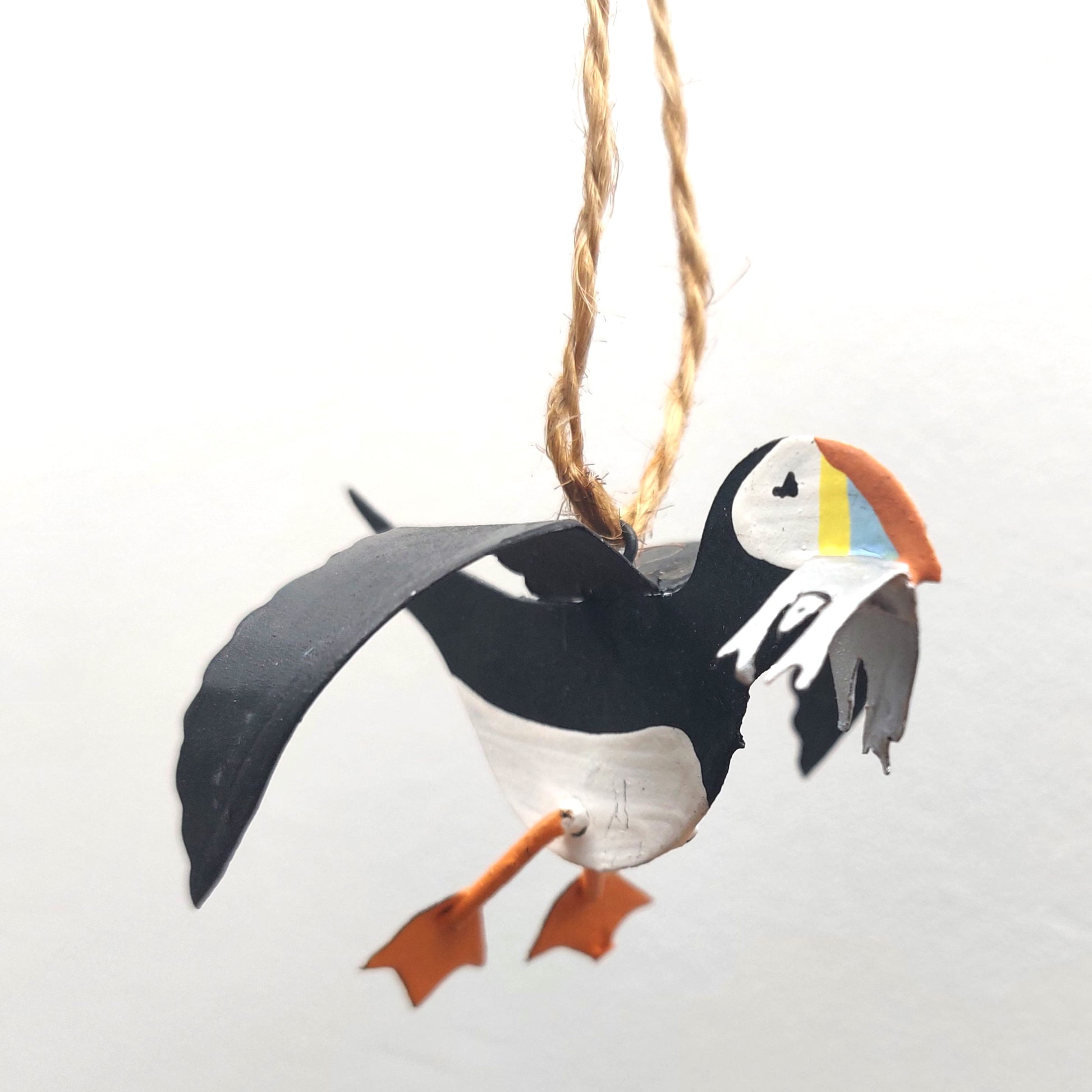 Metal hand painted puffin ornament with some metal sand eels hanging on twine against a white background