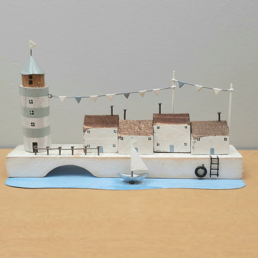 A scene depicting a lighthouse, buildings and a boat on a quayside as an ornament