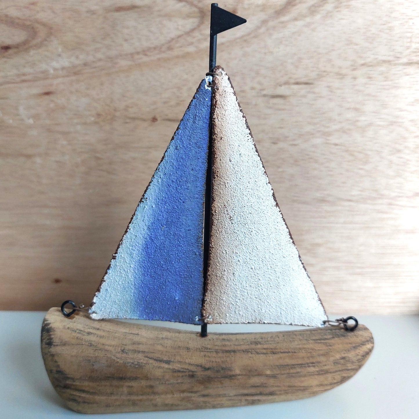 Wooden and metallic sailboat model with blue and white sails on a wooden background