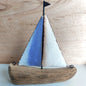 Wooden and metallic sailboat model with blue and white sails on a wooden background