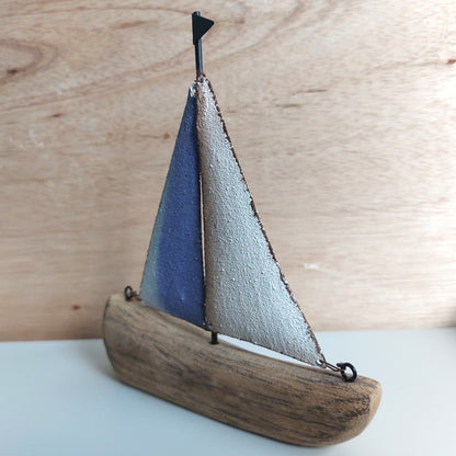 Small sailboat wooden and metal model with wooden base, blue and white sails on a light wood background
