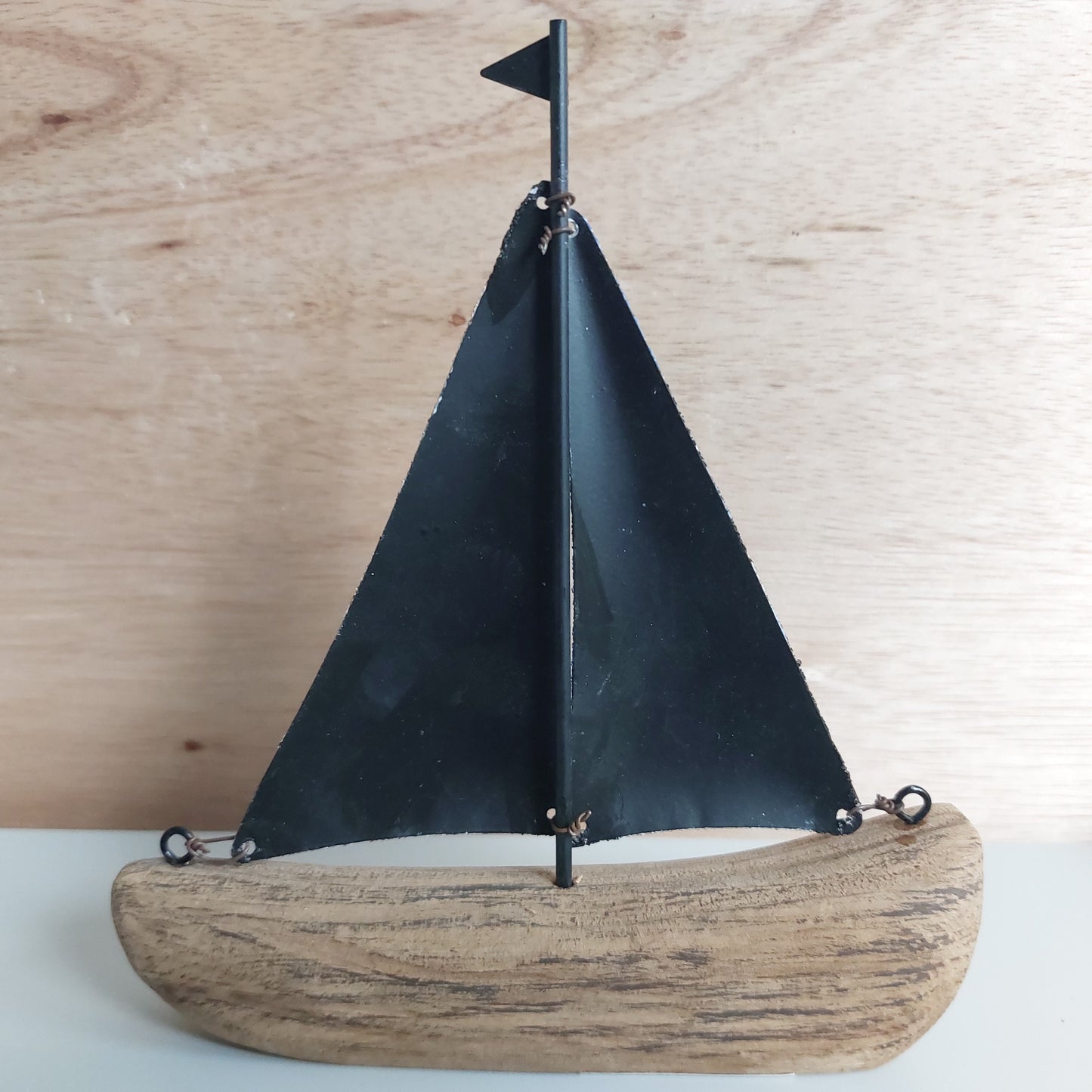 Model wooden and metal sailboat with a black sail on a wooden surface
