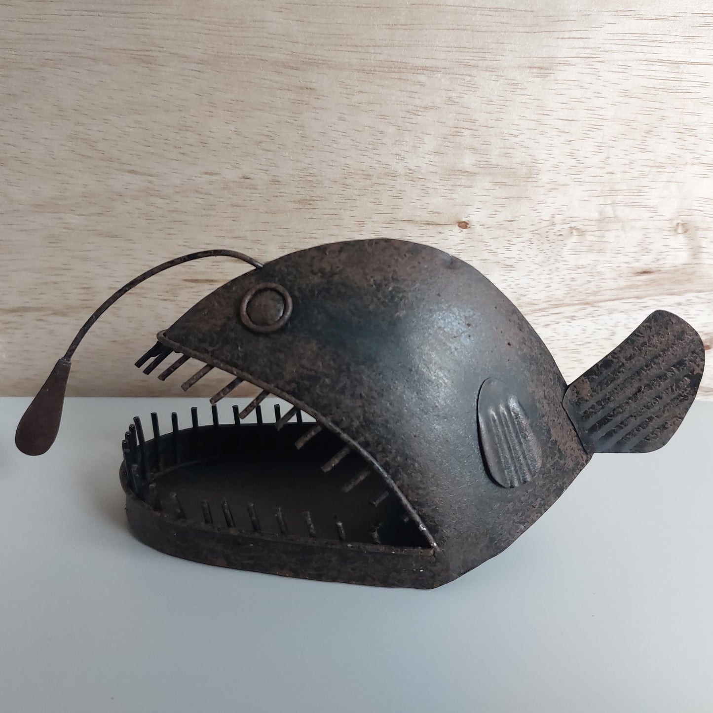 Decorative metal angler fish sculpture on a wooden surface