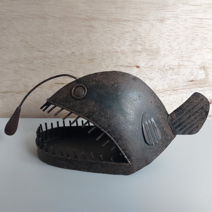 Decorative metal angler fish sculpture on a wooden surface